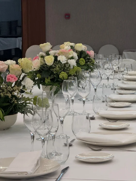 Festlich eingedeckte Tafel mit Blumengestecken, Weingläsern und weißen Stuhlhussen