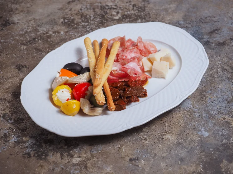 Antipasti-Teller mit Oliven, gefüllter Paprika, Salami, Parmesan, getrockneten Tomaten und Grissini